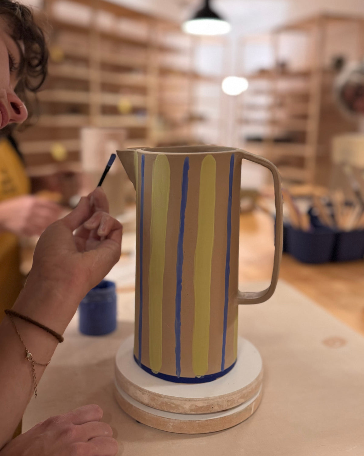 Décoration au pinceau d’un grand pichet en céramique à rayures bleues et jaunes pendant un atelier.