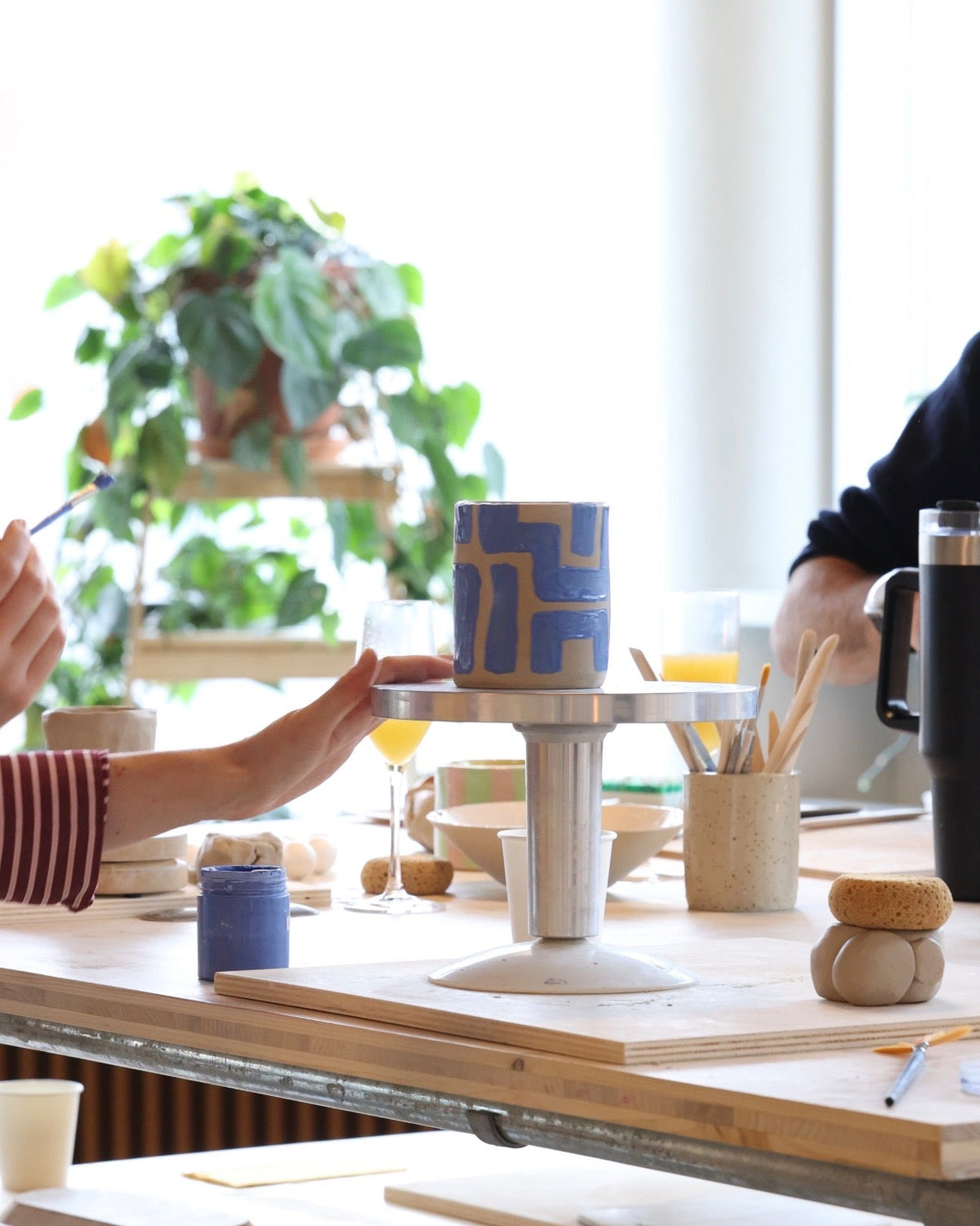 Décoration d’un mug en céramique à motifs géométriques bleus sur une tournette pendant un atelier.