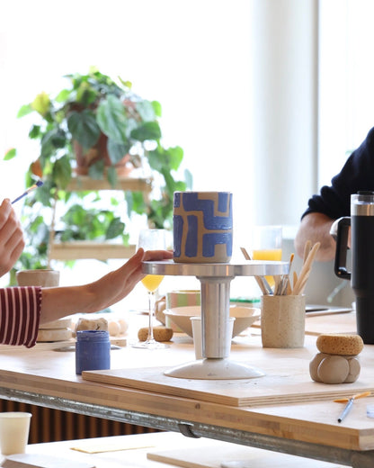 Décoration d’un mug en céramique à motifs géométriques bleus sur une tournette pendant un atelier.