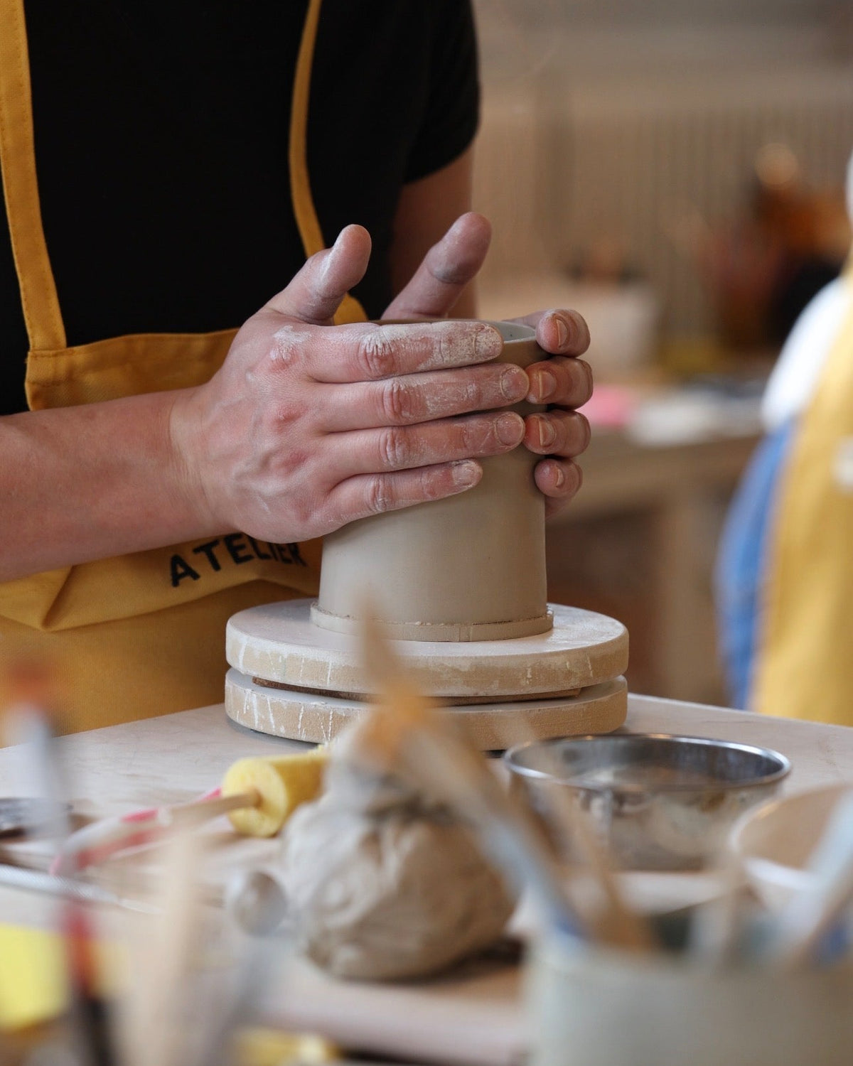 Mains façonnant un mug en argile sur une tournette pendant un cours de poterie.