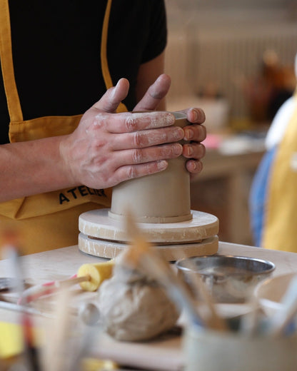 Mains façonnant un mug en argile sur une tournette pendant un cours de poterie.